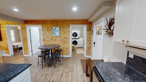 A compact kitchen with granite countertops, a dining area with a round table and stools, and a laundry room with a washing machine and dryer. - Secluded modern cabin, with hot tub (Logan)