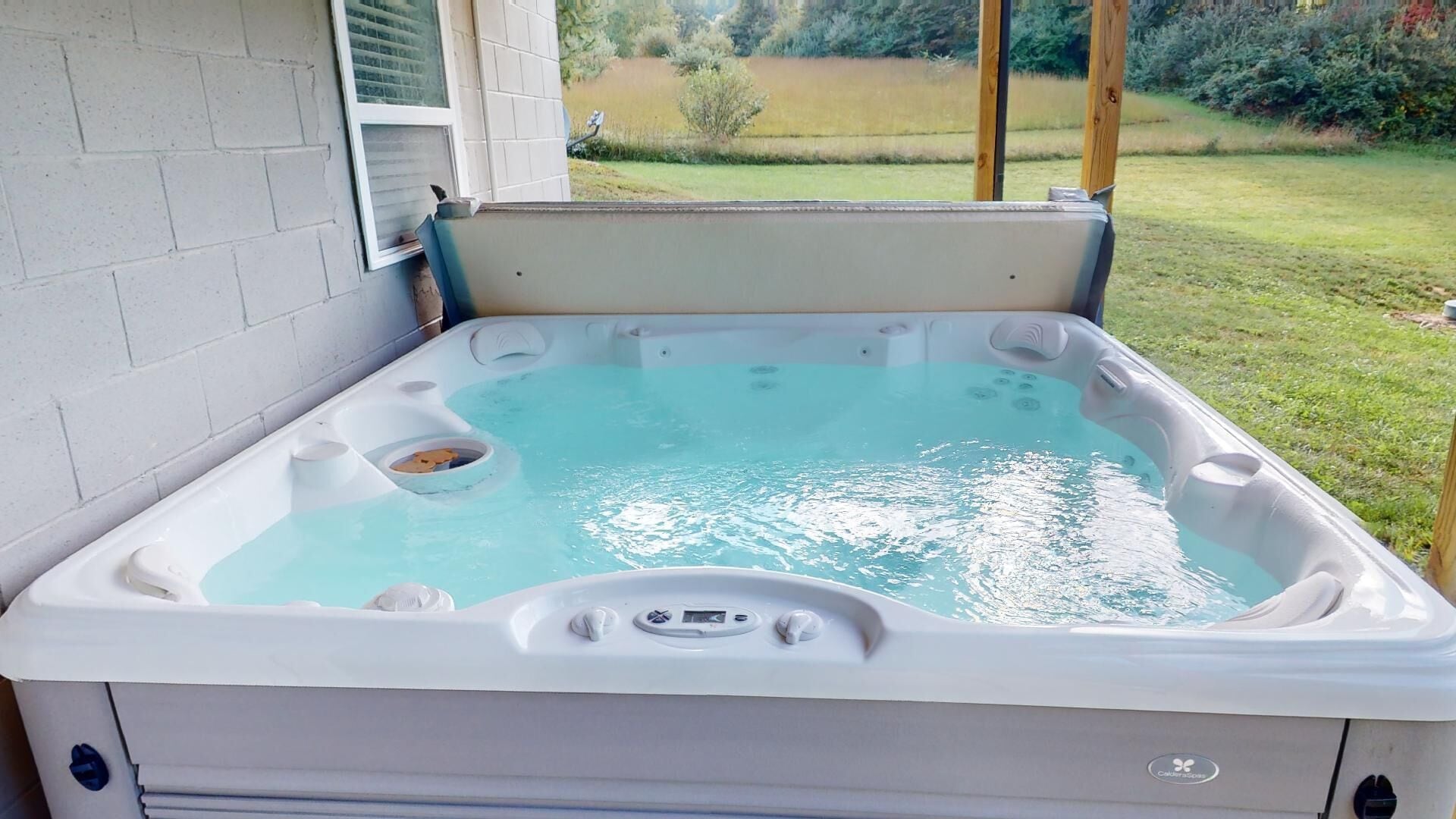 A hot tub with a control panel, a drain, and a view of a garden.