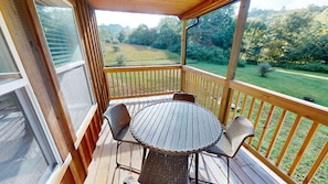Une terrasse extérieure couverte, dotée d’une table ronde et de quatre chaises, qui offre une vue sur une pelouse et des arbres.