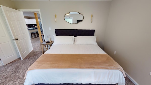 Une chambre à coucher comprenant un lit, une table de chevet, un miroir et une porte donnant sur la cuisine.
