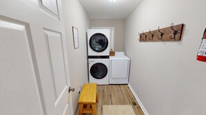 A laundry room with stacked washers and dryers, a wooden bench, and a coat rack.