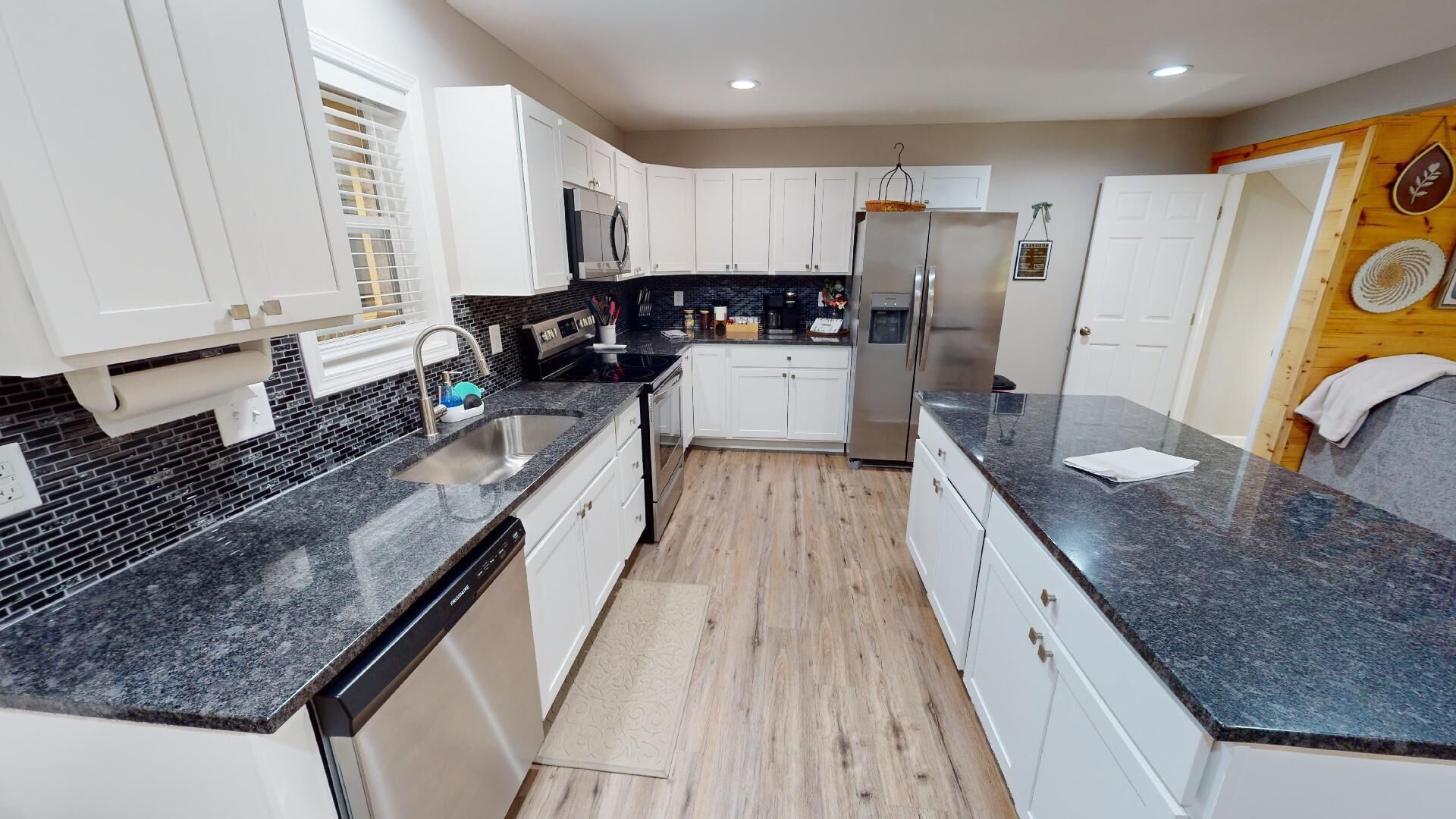 A modern kitchen with white cabinets, black countertops, and stainless steel appliances.