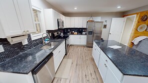 A modern kitchen with white cabinets, black countertops, and stainless steel appliances.