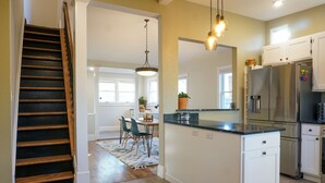 Una cocina con isla central, muebles blancos, electrodomésticos de acero inoxidable y una zona de comedor con sillas y mesa.