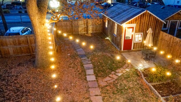 Una pequeña cabaña de madera con una puerta roja, rodeada por un sendero de piedra e iluminada por luces colgantes.