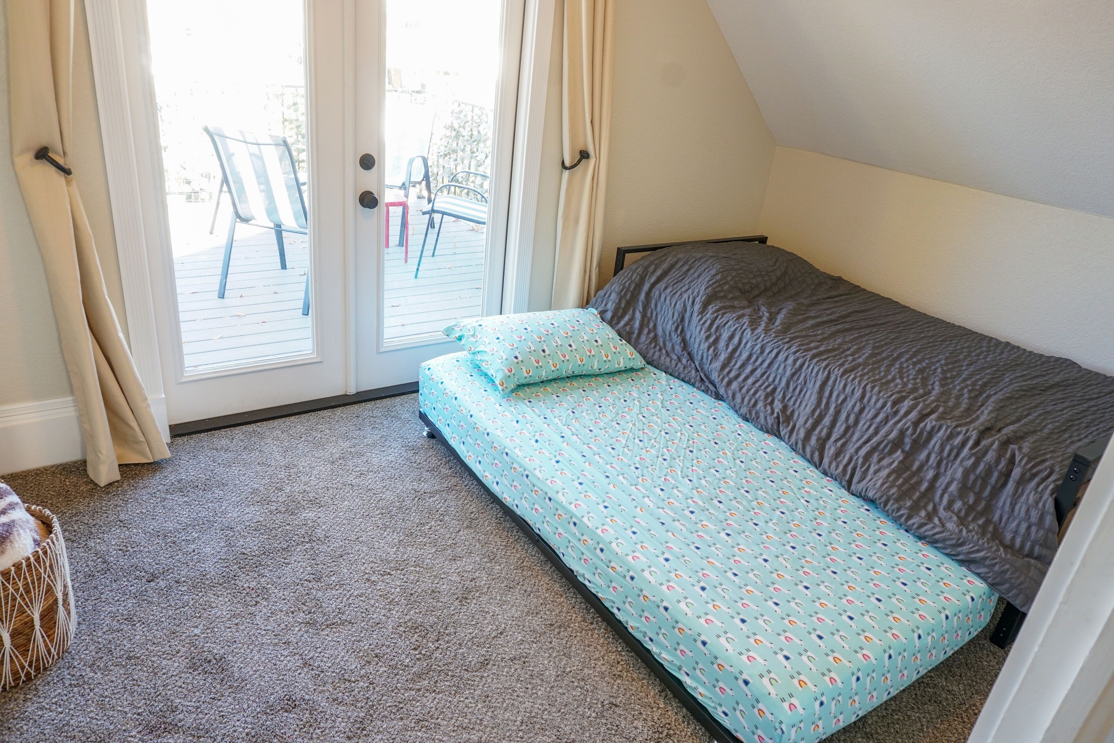 Un dormitorio con una cama individual, una ventana con cortinas y vistas a muebles de exterior.