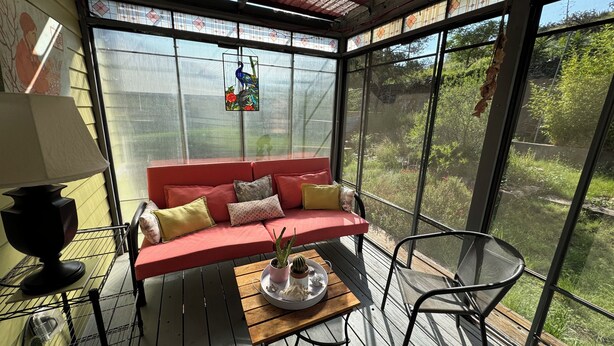 Un invernadero con un sofá rojo, una mesa de madera con una bandeja de plantas y una silla.