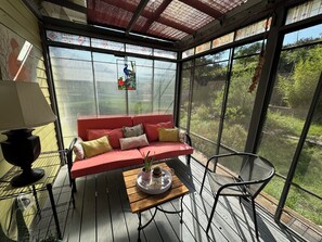 A conservatory with a red sofa, a wooden table with a tray of plants, and a chair. - Bungalow in Old Bisbee (Bisbee)