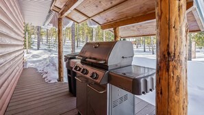 Un espace barbecue extérieur abrité, doté d’une terrasse en bois et recouvert de neige.