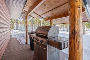 A covered outdoor grill area with a wooden deck and snow on the ground. - Stanley Stays - The Bonanza Cabin (Stanley)