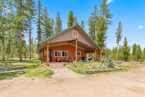 A cabin with a porch, outdoor seating, and a view of the surrounding forest. - Stanley Stays - The Bonanza Cabin (Stanley)