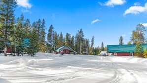 Un paysage enneigé avec une cabane rouge et un bâtiment au toit bleu, entourés de grands arbres.