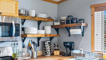 A kitchen with a built-in microwave, stainless steel appliances, wooden shelves with dishes, and a coffee maker.