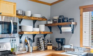 A kitchen with a built-in microwave, stainless steel appliances, wooden shelves with dishes, and a coffee maker. - Stanley Stays - The Bonanza Cabin (Stanley)