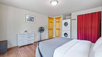 A bedroom with a bed, a washing machine, a fan, and a dresser.