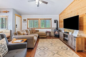 A cabin interior with a sofa, a television, a fireplace, and a window with blinds. - Stanley Stays - The Bonanza Cabin (Stanley)