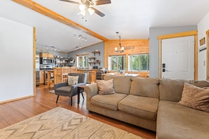A modern kitchen with wooden cabinets, a dining area with a sofa, and a large window offering a view of the outdoors.