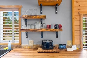 A kitchen with wooden shelves holding glasses and mugs, a toaster, and a digital scale.