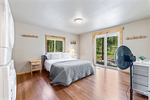 A bedroom with a bed, a nightstand, a lamp, a fan, and a view of the outdoors through a sliding door.