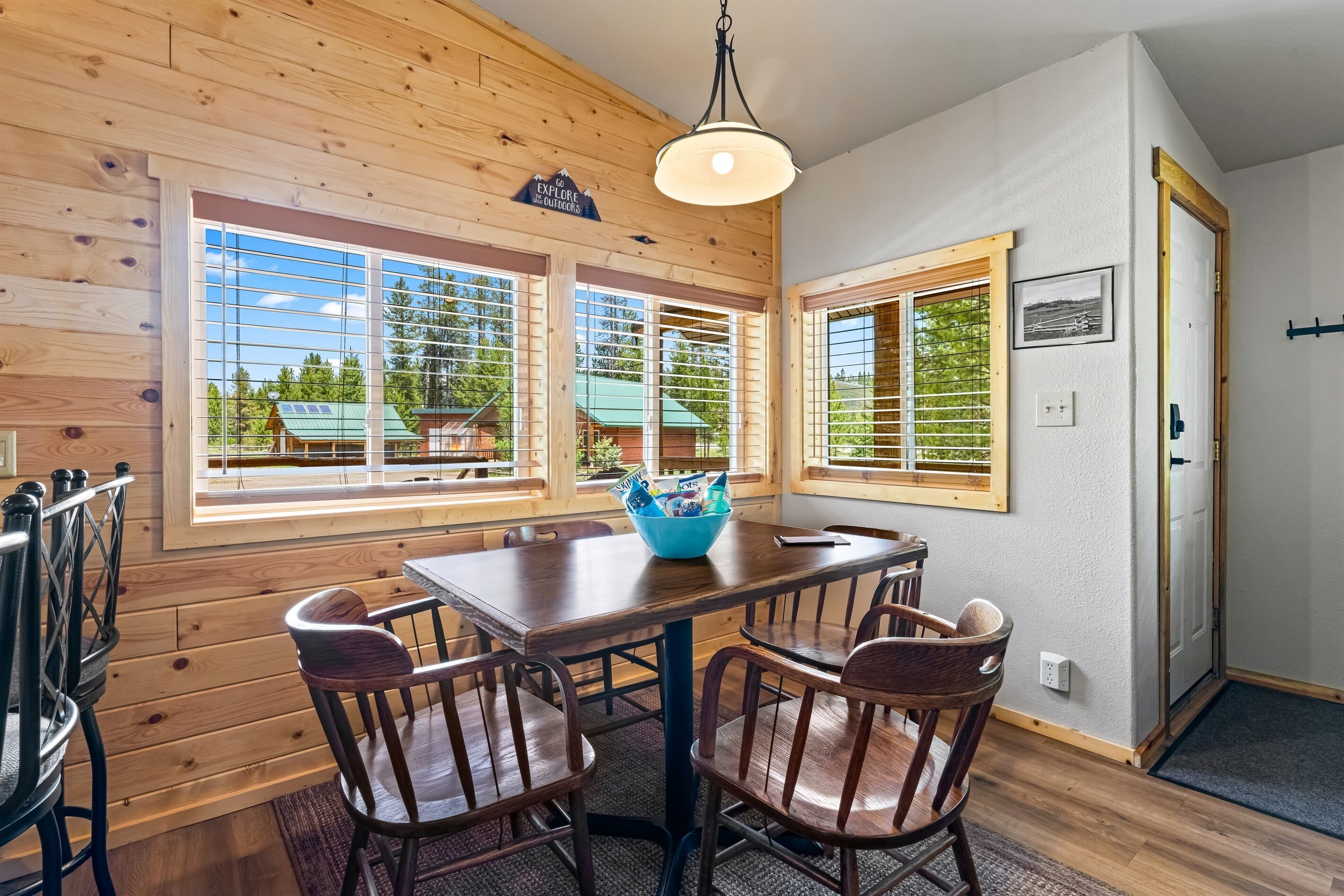 A wooden interior with a dining table and chairs, large windows with blinds, and a door with a sign.