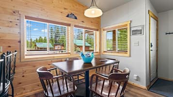 A wooden interior with a dining table and chairs, large windows with blinds, and a door with a sign.