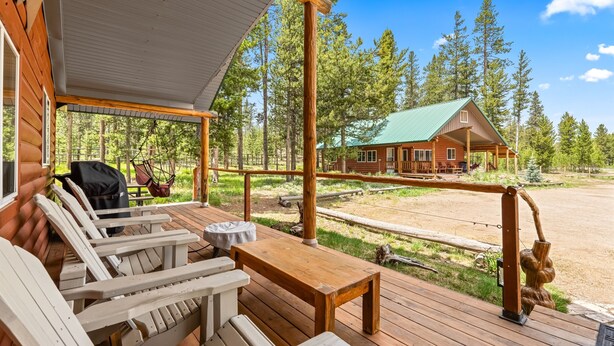 A wooden deck with outdoor seating and a view of a cabin in a forest. - Stanley Stays - The Ponderosa Pine Cabin (Stanley)