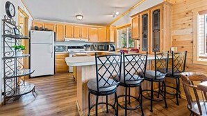 A kitchen with wooden cabinets, a white refrigerator, a stove, and a bar area with stools. - Stanley Stays - The Ponderosa Pine Cabin (Stanley)