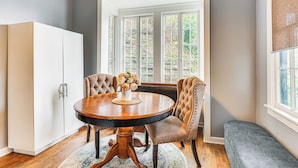 A dining area with a round table, two upholstered chairs, a bench, and a white cabinet. - Cozy Eureka Springs Cottage, Walk to Dtwn! (Eureka Springs)