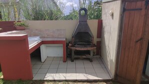 Un patio con una parrilla, una mesa pequeña y plantas en macetas.