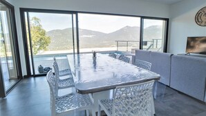 Un moderno comedor con una mesa de vidrio y sillas blancas, con vistas a un paisaje montañoso.