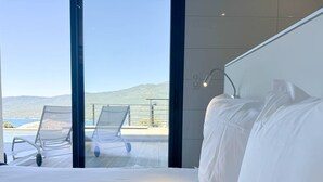 Habitación de hotel con una cama grande, vista al mar y dos sillones en un balcón.