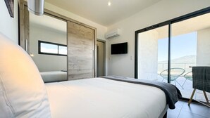 Un dormitorio moderno con una cama grande, puerta corredera, televisor y balcón con sillas.
