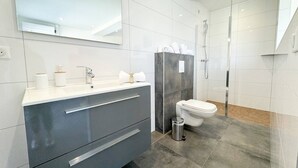 Un baño moderno con un espejo grande, un tocador con lavabo, inodoro y zona de ducha.
