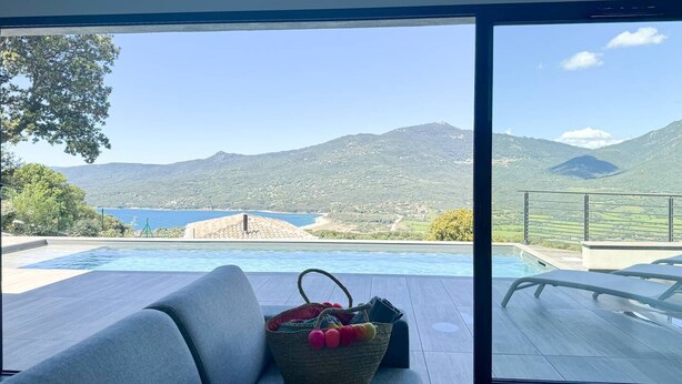 Una habitación moderna con un amplio ventanal corredera que da a una zona de piscina y vistas a la montaña.