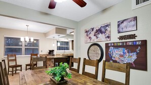 Un coin repas avec une table en bois, des chaises et une plante en pot. Les murs sont décorés, notamment avec une carte des États-Unis et une citation.