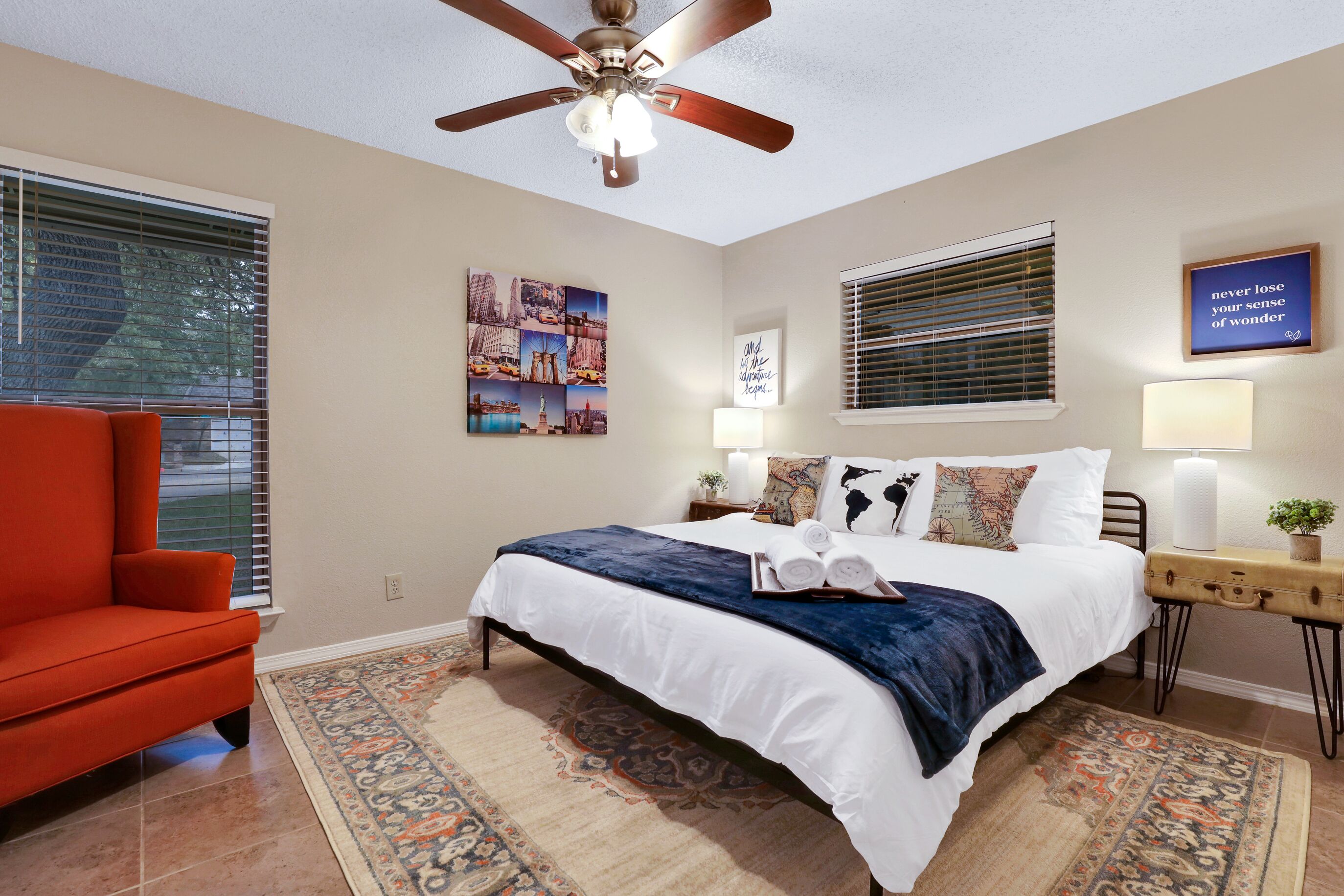 A bedroom with a bed, a red chair, a ceiling fan, and a wall with a poster and a sign.