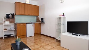 A compact kitchen with wooden cabinets, a white refrigerator, a coffee maker, and a TV on a stand. - Sea Waves - 500M from the beach, Pool and Terrace By LVH (Puerto del Carmen)