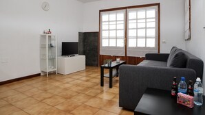 A living room with a gray sofa, a white entertainment unit, a TV, and a small table with a plant. - Sea Waves - 500M from the beach, Pool and Terrace By LVH (Puerto del Carmen)