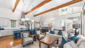 A spacious living area with a large wooden beam ceiling, a kitchen with white cabinets, and a dining area with a chandelier. - Bon Temps | 5 Bedroom w/Private Pool (Rosemary Beach)