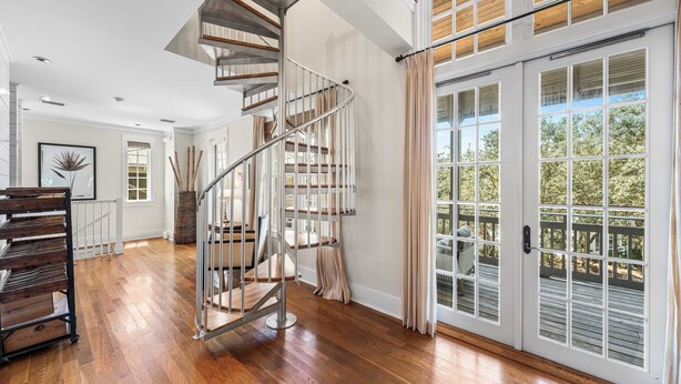 A spacious room with a wooden floor, a spiral staircase, and a large sliding glass door leading to an outdoor deck. - Bon Temps | 5 Bedroom w/Private Pool (Rosemary Beach)