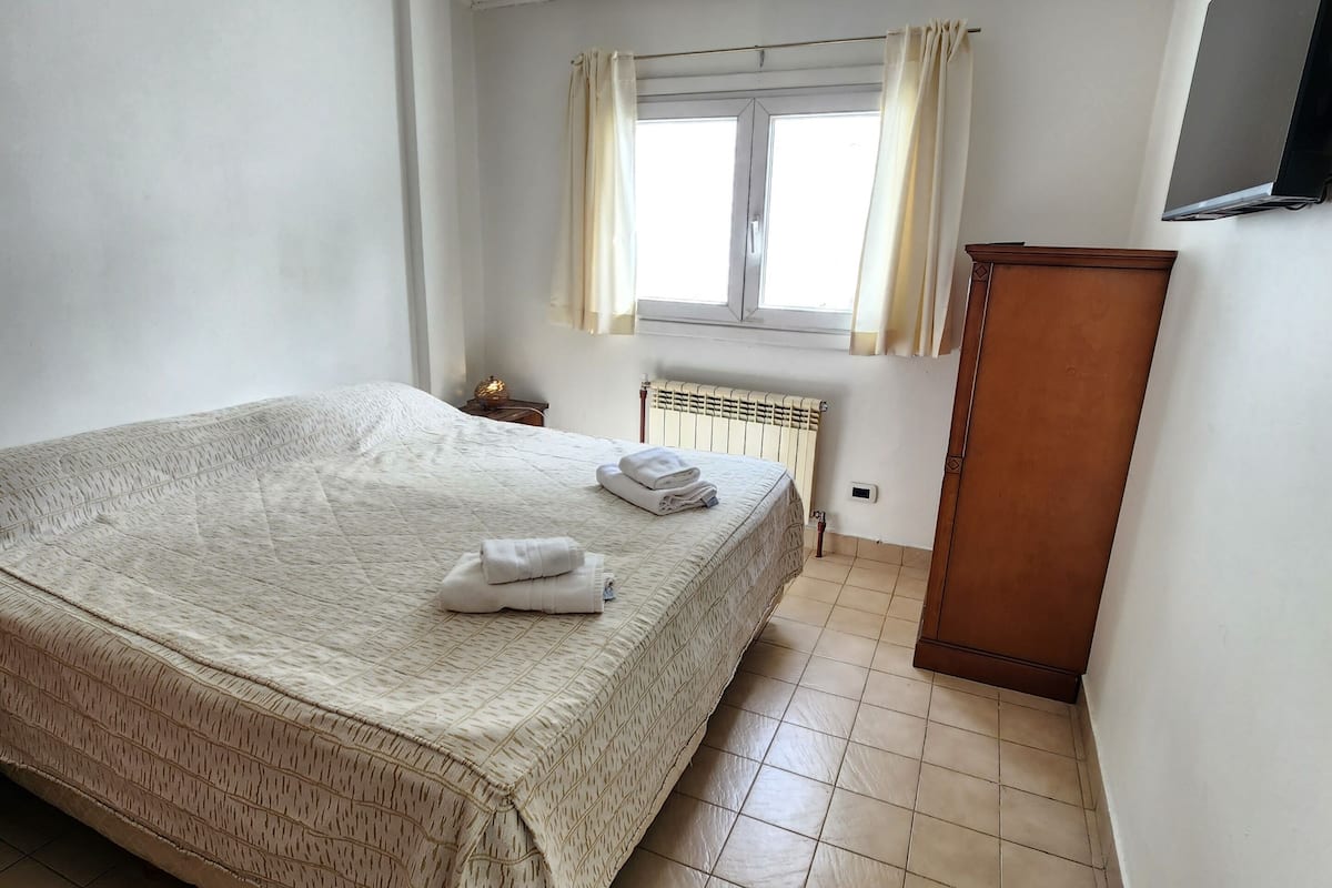 A bedroom with a bed, a radiator, a wooden wardrobe, and a window with curtains.