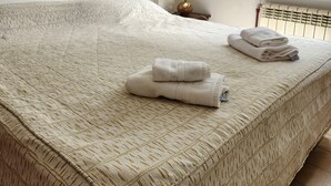 A neatly made bed with a patterned bedspread, a folded towel, and a small bedside table with a decorative item. - Anum Hostel (Ushuaia)