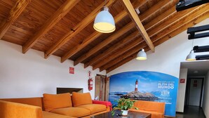 A spacious room with a high wooden ceiling, orange sofas, a white ottoman, and a tiled floor. - Anum Hostel (Ushuaia)