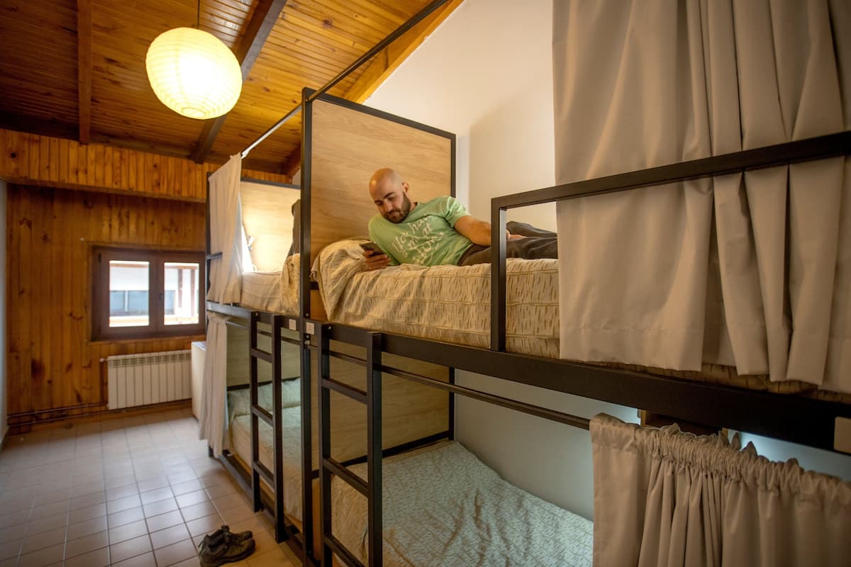 A bunk bed room with a wooden ceiling, a window with curtains, and a radiator.