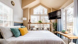 A bedroom with a large bed, a TV, a desk, and a window with a view. - Cozy 1BR Chalet | Pikes Peak, Grill & Relaxing Patio (Woodland Park)