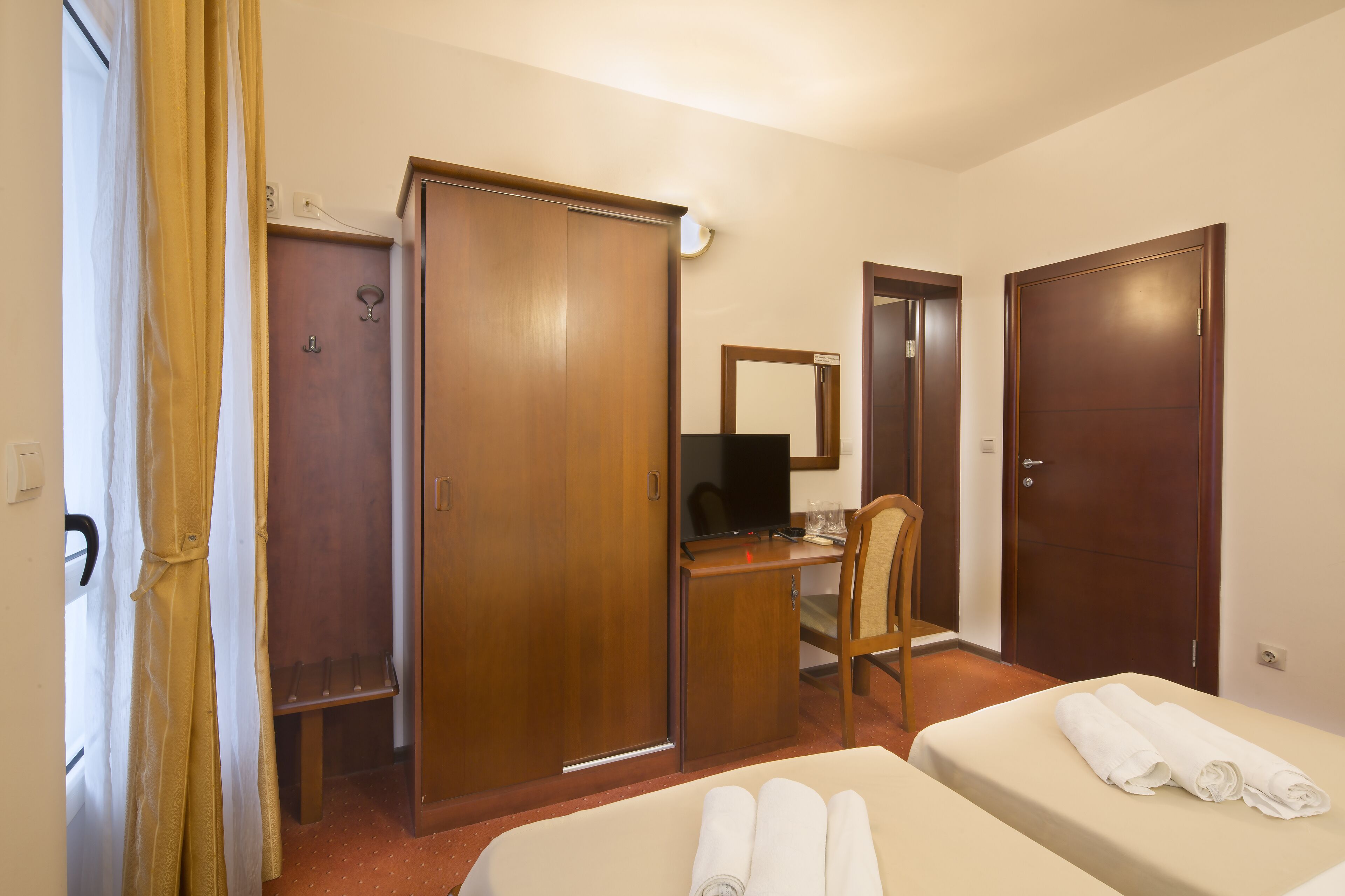A hotel room with a bed, a desk, a chair, a wardrobe, and a bathroom.
