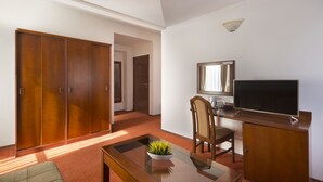 Habitación de hotel con un armario corredero de madera, un televisor de pantalla plana sobre un mueble de madera, una mesa de centro de cristal con una planta y una silla de madera.