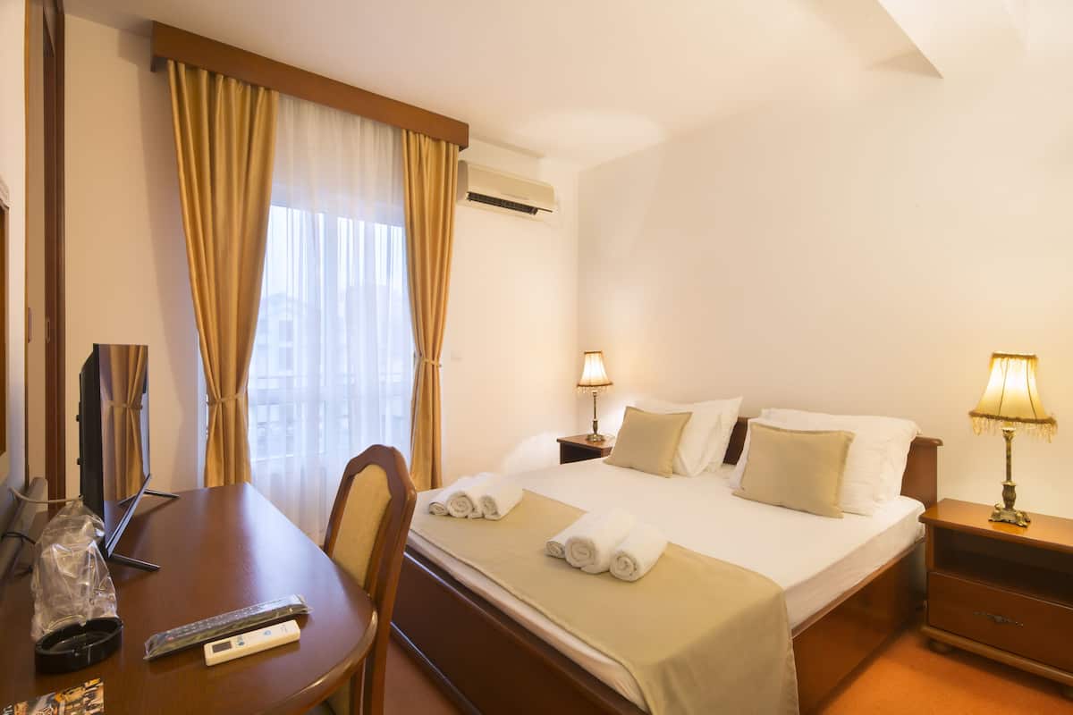 A hotel room with a bed, bedside tables, a desk with a chair, a TV, and curtains.