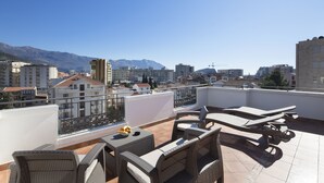 Una terraza en la azotea con mobiliario exterior, vistas a la ciudad y montañas al fondo.