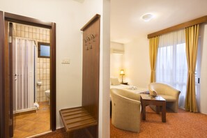 Habitación de hotel con puerta de madera, una cama, una silla, una mesa y ventana con cortinas.